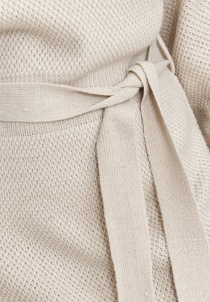 Beżowy dziany element odzieży z teksturowanym wzorem, z paskiem w talii i gładkim wykończeniem na brzegach.