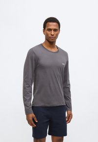 Long-sleeve grey shirt made of soft fabric with a crew neck; features a small white logo on the chest, paired with navy shorts.