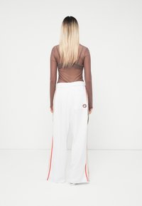 Long-sleeved sheer brown top paired with white wide-leg pants featuring multicolored side stripes and a back pocket with logo detail.