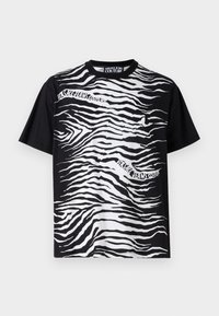 Fekete póló, fehér zebra csíkos mintával, rövid ujjakkal és fehér logós szöveggel. Pamut anyag, laza illeszkedés.