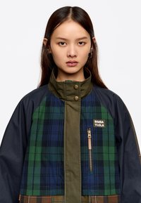 Jakna v barvnih blokih s kombinacijo modrih, zelenih in bež karo vzorcev, z zadrgo žepom in gumbom na zaklep.