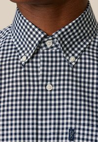 Camicia a maniche corte con bottoni in motivo a quadri navy e bianco. Presenta un colletto alla francese e due bottoni bianchi al collo. Tessuto morbido.