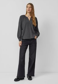 Gray striped long-sleeve blouse with a V-neck, featuring a relaxed fit and gathered cuffs, worn with high-waisted black wide-leg pants.
