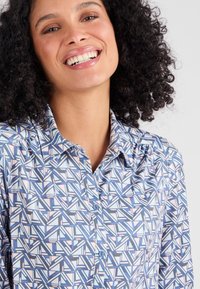 Camicia a motivi blu e rosa con colletto, chiusura con bottoni e tessuto texturizzato con forme geometriche.