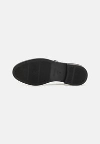 Black shoe sole with a textured surface, featuring a rectangular pattern and a strap across the arch. Marked with brand and size details.