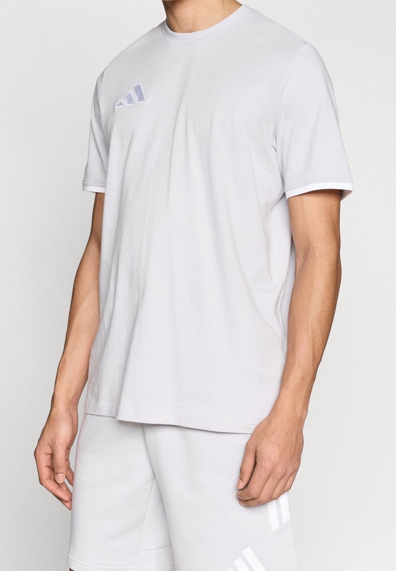 Homme portant un t-shirt à manches courtes gris clair uni et un short assorti avec un logo Adidas discret sur la poitrine et la jambe.