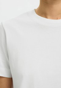 Gros plan d'une personne portant un T-shirt blanc uni à col rond et à manches courtes, avec une texture de tissu lisse.