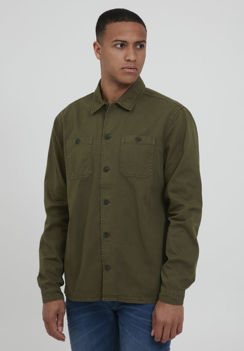 Olive green button-up shirt made of durable fabric, featuring two chest pockets, black buttons, and a collar. Long sleeves extend to the wrists.