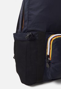 Granatowy plecak posiada teksturowaną, czarną siatkową boczną kieszeń, jasne wielokolorowe akcenty zamków oraz trwałą konstrukcję z tkaniny.
