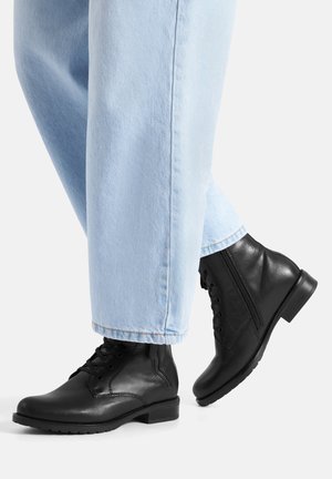 Czarne skórzane botki na płaskim obcasie, z wiązaniem i zamkiem błyskawicznym z boku, zestawione z jasnoniebieskimi jeansami o szerokich nogawkach.