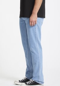 Jeans in denim azzurro chiaro con taglio dritto e dettagli di sbiaditura leggera, abbinati a sneaker nere in tela e una t-shirt nera.