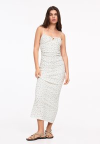 Rochie midi florala cu bretele ajustabile, dintr-un material crem deschis, cu un centru volant și un model cu flori albastre dispersate. Purtați cu sandale.