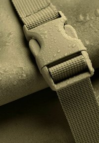 Cintura in nylon verde con superficie texture, dotata di una fibbia in plastica grigia. Le gocce d'acqua sul tessuto evidenziano la sua resistenza all'umidità.