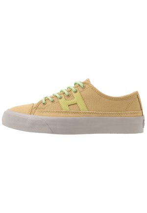 Low-top beige canvas sneaker with light green laces and side logo, thick white rubber sole, side view on white background.