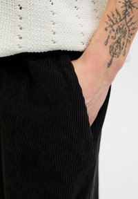 Sorte fløjl bukser med en struktureret overflade, der har en sidelomme. Stoffet har lodrette ribber, hvilket forbedrer det overordnede design.