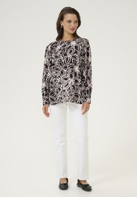 Langärmlige Bluse mit einem schwarzen und hellrosa Blumenmuster, Rundhalsausschnitt und lässiger Passform. Kombiniert mit weißen Hosen und schwarzen Ballerinas.