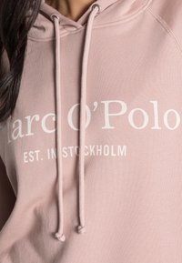 Felpa rosa realizzata in tessuto morbido, con cappuccio regolabile e stampa bianca "Marc O'Polo EST. A STOCCOLMA" sul davanti.