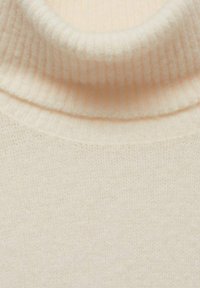 Maglione color crema con un collo a dolcevita a costine e una superficie liscia. La vista ravvicinata mostra il tessuto morbido con un fine motivo a maglia.