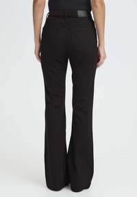 Jeans de campana negros con cintura alta, hechos de denim. Presentan dos bolsillos traseros y una etiqueta en la cinturilla, que exhibe un sencillo diseño de costura.