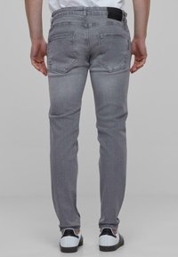 Harmaa farkkuhousu slim fit -mallilla, viidellä taskulla, mustalla merkillä vyötärökappaleessa ja sileällä, hieman teksturoidulla pinnalla.