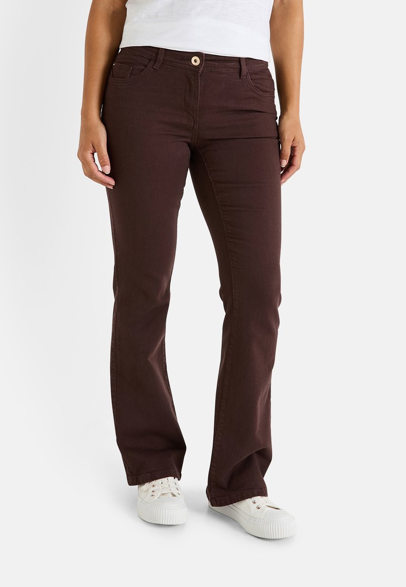 Pantalons évasés en denim marron avec cinq poches, une fermeture à bouton sur le devant et une texture lisse, associés à des baskets blanches.