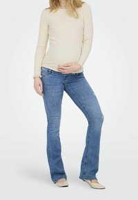 Beige långärmad topp med volangärmar, kombinerad med ljusblå utsvängda jeans som har lätt slitningar och designade bakfickor. Neutrala ballerinaskor.