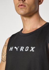 Zwart mouwloos sporttop gemaakt van gladde stof, met een witte bedrukte logo "HYROX" over de borst, en een ronde halslijn.