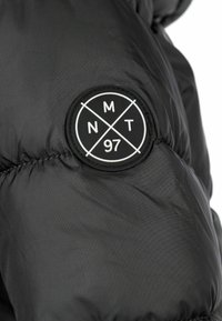 Čierna puffová bunda s okrúhlou nášivkou a bielym nápisom "NMT 97" a krížovým dizajnom. Textúrovaná, hladká látka s prešitými detailmi.