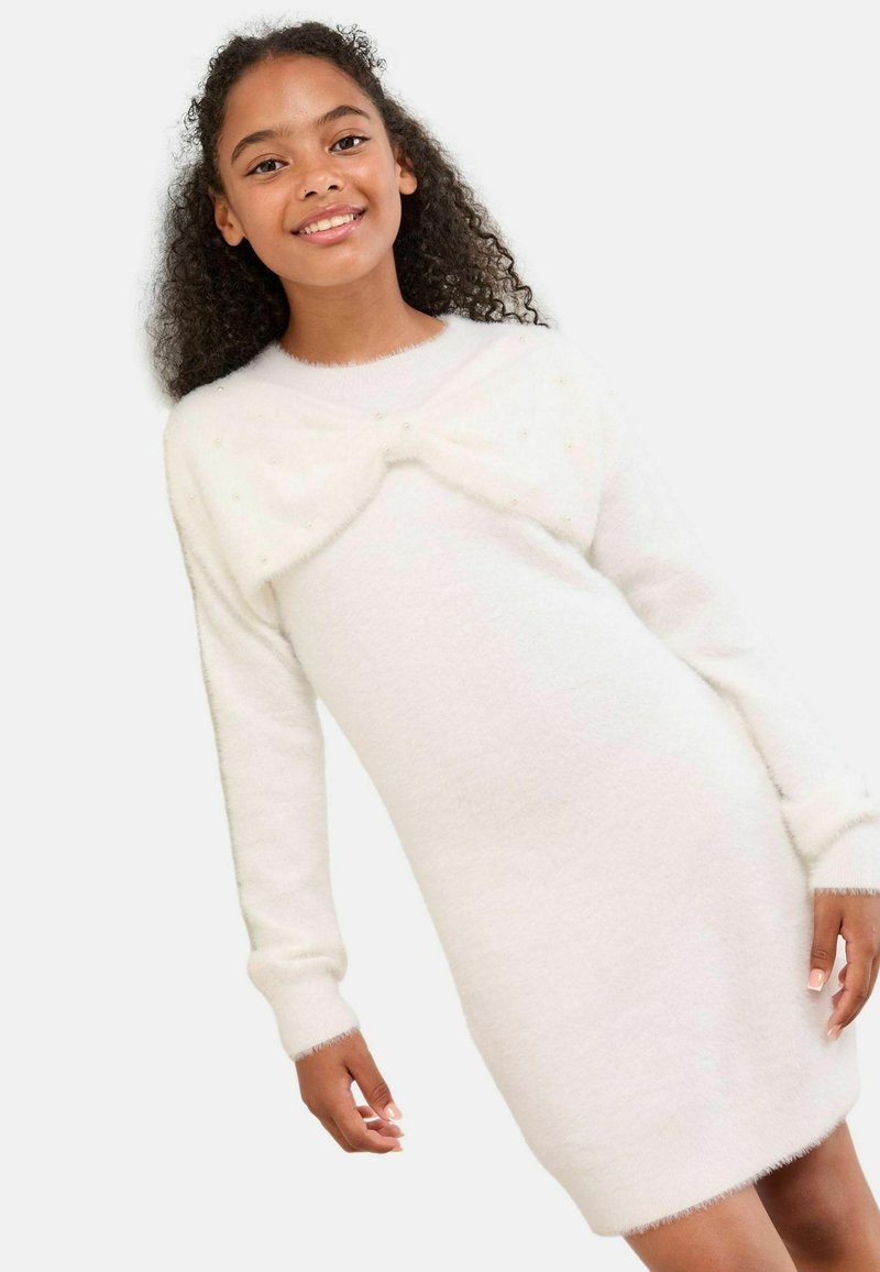 Weißes gestricktes Kleid mit langen Ärmeln, weichem Material und einer Schleifen-Detail am Ausschnitt, akzentuiert mit kleinen, funkelnden Verzierungen.