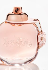 Clear glass perfume bottle with a rounded shape, pink liquid inside, rose gold cap, embossed horse and carriage design, and floral charm.