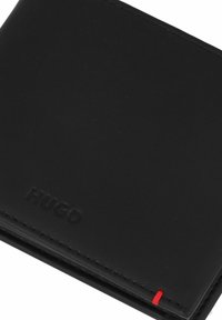 Portafoglio in pelle nera con logo "HUGO" impresso. Presenta una cucitura rossa a contrasto e un design elegante e minimale.