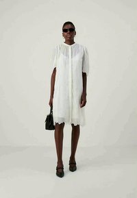 Λευκό λινοφόρεμα με φουσκωτά μανίκια, κομμένη βάση και κουμπιά μπροστά. Σε συνδυασμό με μαύρη τσάντα και παπούτσια. Λείο υλικό.