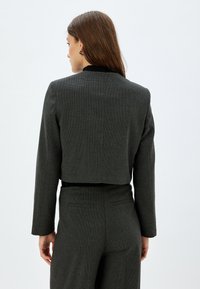 Grijze cropped blazer met een gestructureerd patroon, op maat gemaakt pasvorm en contrasterende zwarte kraagdetails. Beschikt over lange mouwen en een nette afwerking.