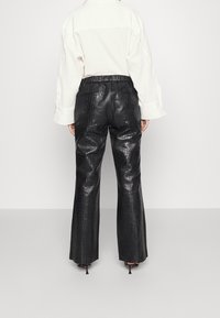 Zwarte nep leren broek met een textuur van krokodillenleer; wijd pijp ontwerp; elastische tailleband; gecombineerd met een witte overhemden.