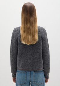 Suéter gris de punto con textura acanalada y manga larga, combinado con jeans de mezclilla azules. Vista desde la parte posterior, mostrando cabello hasta los hombros.