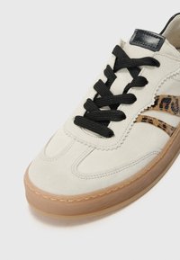 Casualne buty z beżową zamszową cholewą, czarnymi sznurówkami, leoparda wzorem po bokach i gumową podeszwą. Teksturowany design z zakrzywionymi szwami.