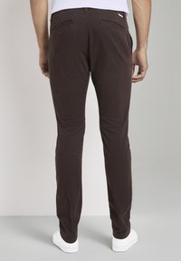 Pantaloni di cotone marroni con vestibilità slim e due tasche posteriori, abbinati a sneakers bianche. Tessuto liscio e linee pulite.