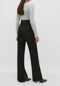 Pantalon noir à larges jambes avec fentes latérales, associé à un pull gris côtelé ajusté. Le pantalon présente une taille haute et un tissu fluide.