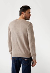 Pull en tricot beige clair avec des éclats d'orange subtils, col rond, poignets et ourlet côtelés. Associé à un jean bleu foncé avec des coutures contrastantes.