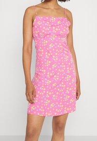 Pink sleeveless dress with a floral pattern featuring yellow and blue flowers. Fitted design, smooth fabric, and a straight hem.