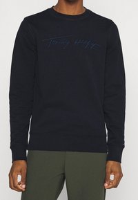 Marineblauwe sweatshirt met ronde hals, voorzien van een opgestikt geborduurd "Tommy Hilfiger"-logo over de borst. Katoenen materiaal, ribgebreide manchetten.