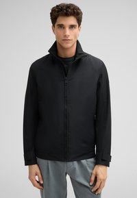 Schwarze Zip-Up-Jacke mit hohem Kragen, weicher Textur und minimalistischen Design. Verfügt über eine taillierte Passform und subtile Nähte.