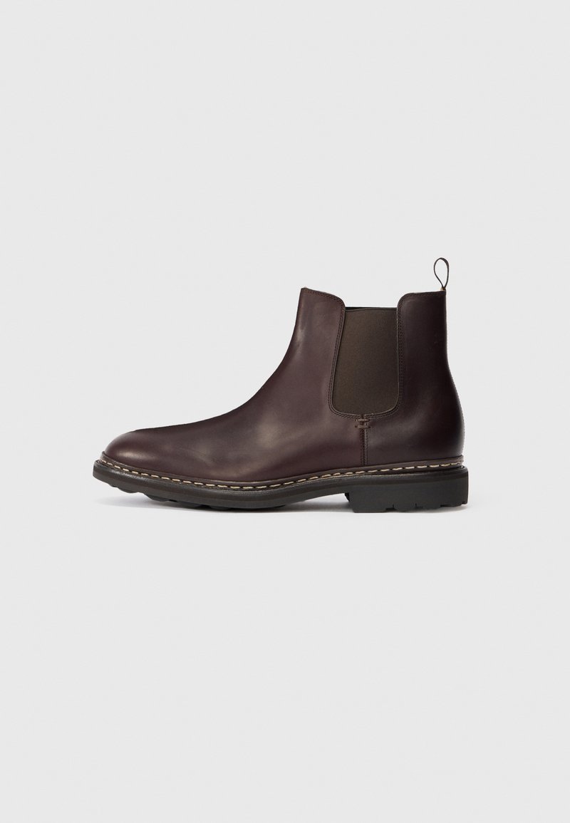 Bottines Chelsea en cuir brun foncé avec panneaux latéraux élastiques, tirette au talon et semelle épaisse cousue sur un fond uni.