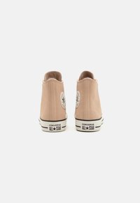 Zapatillas altas de ante beige con suelas de goma blanca, toques en negro y un parche redondo con el logo en cada talón. Diseño clásico de Converse All-Star.