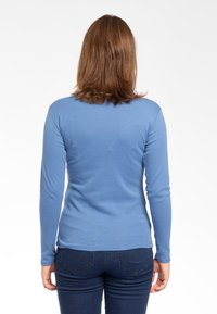 Maglietta aderente a maniche lunghe di colore blu, realizzata in tessuto morbido. Presenta un colletto tondo e una texture liscia, abbinata a jeans scuri.