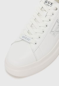 Fehér sneaker sima bőr felülettel, texturált talppal, fehér fűzőkkel és logós címkével. Kiegészítők között ezüst részletek találhatók.