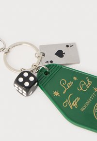 Porte-clés avec une étiquette en plastique verte portant l'inscription dorée "Las Vegas Club" et un numéro de chambre, une carte à jouer en argent et un dé noir à points blancs.