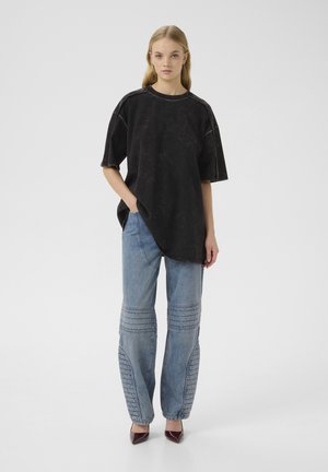 Oversized black t-shirt with shoulder seams and a textured finish, paired with blue denim jeans featuring stitched accents and tapered legs.