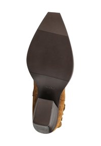 Brązowe zamszowe szpilki damskie pokazane od spodu, z teksturowaną czarną podeszwą i kwadratowym obcasem.