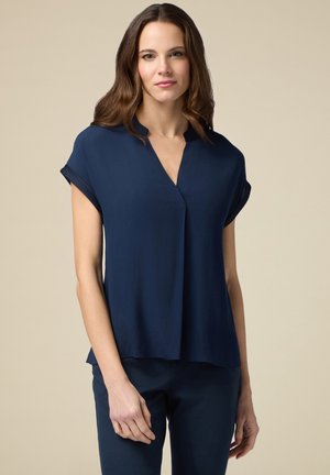 Navyblauwe blouse met een V-hals en korte opgerolde mouwen, met een vloeiende silhout en een zachte textuur. Geen opmerkelijke patronen of hardware.